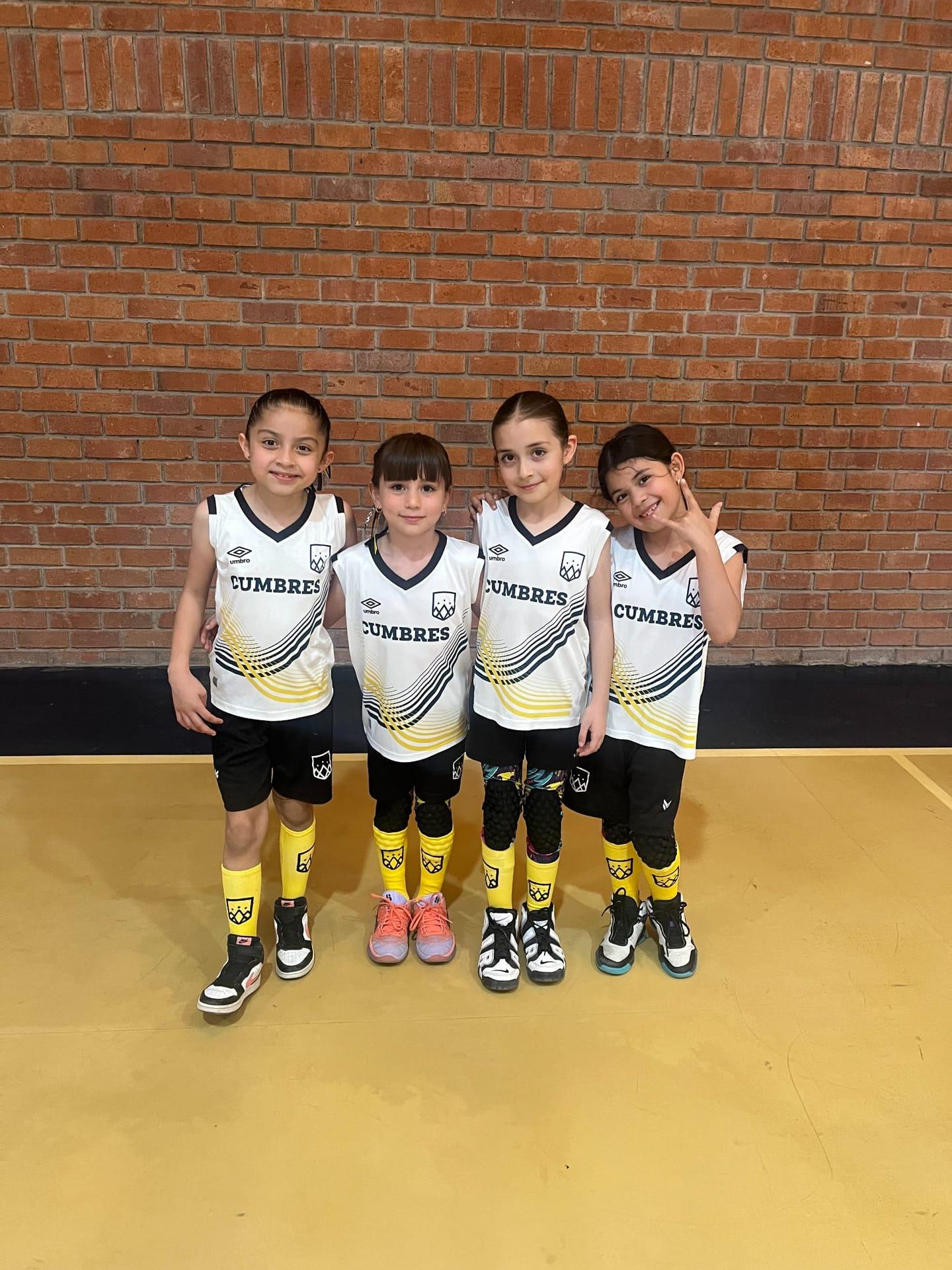 Cuatro estudiantes del Instituto Cumbres con uniforme deportivo amarillo y negro posando juntas en cancha.
